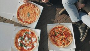 people sitting and eating pizza from pizza boxes