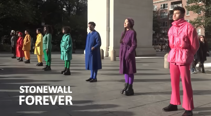 Photo of people dressed in all colors of the rainbow standing in a line. There is type in the bottom left corner that reads "Stonewall Forever"