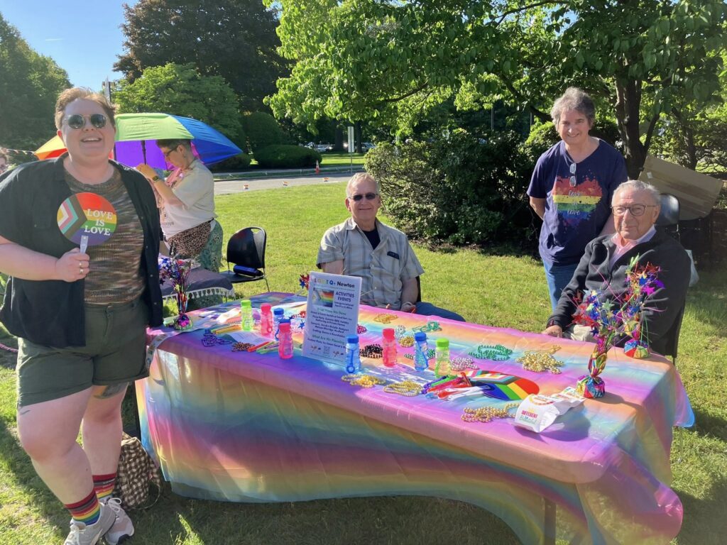 Members of LGBTQ+ Newton posing behind a table at the Newton Flag Raising